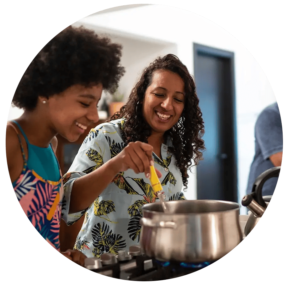 Two ladies stirring a pot on the stove.