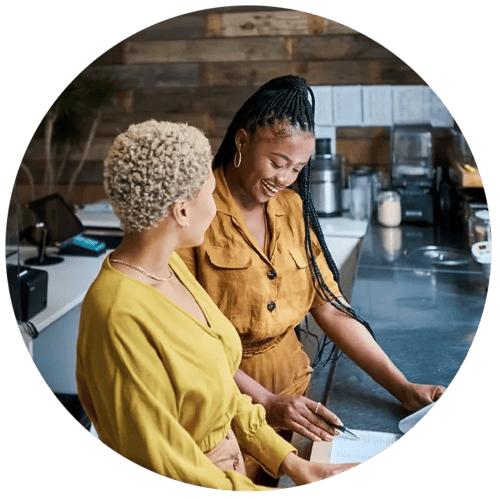 Lady pointing to one item on a paper to another lady. 